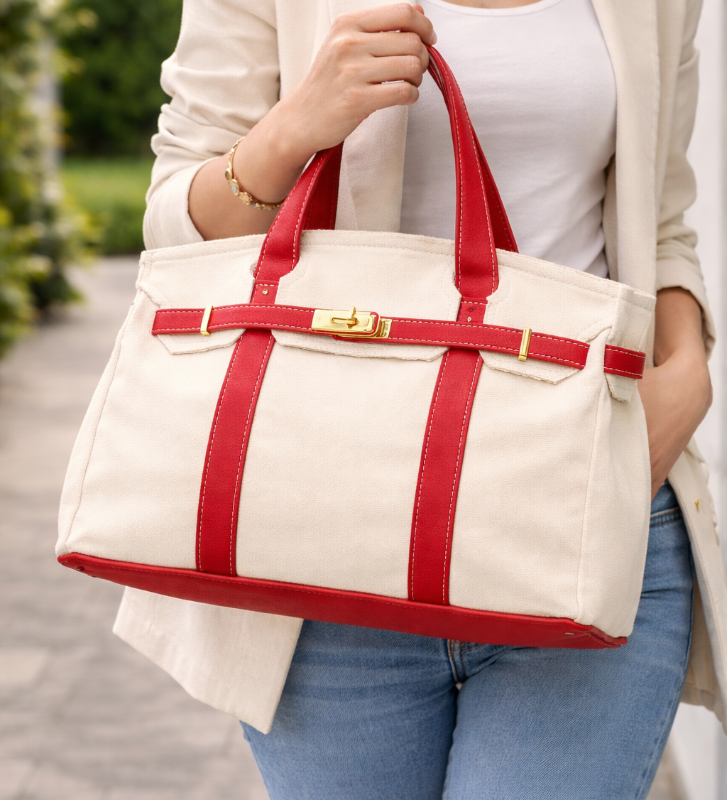 Person holding a white tote bag with red straps outdoors