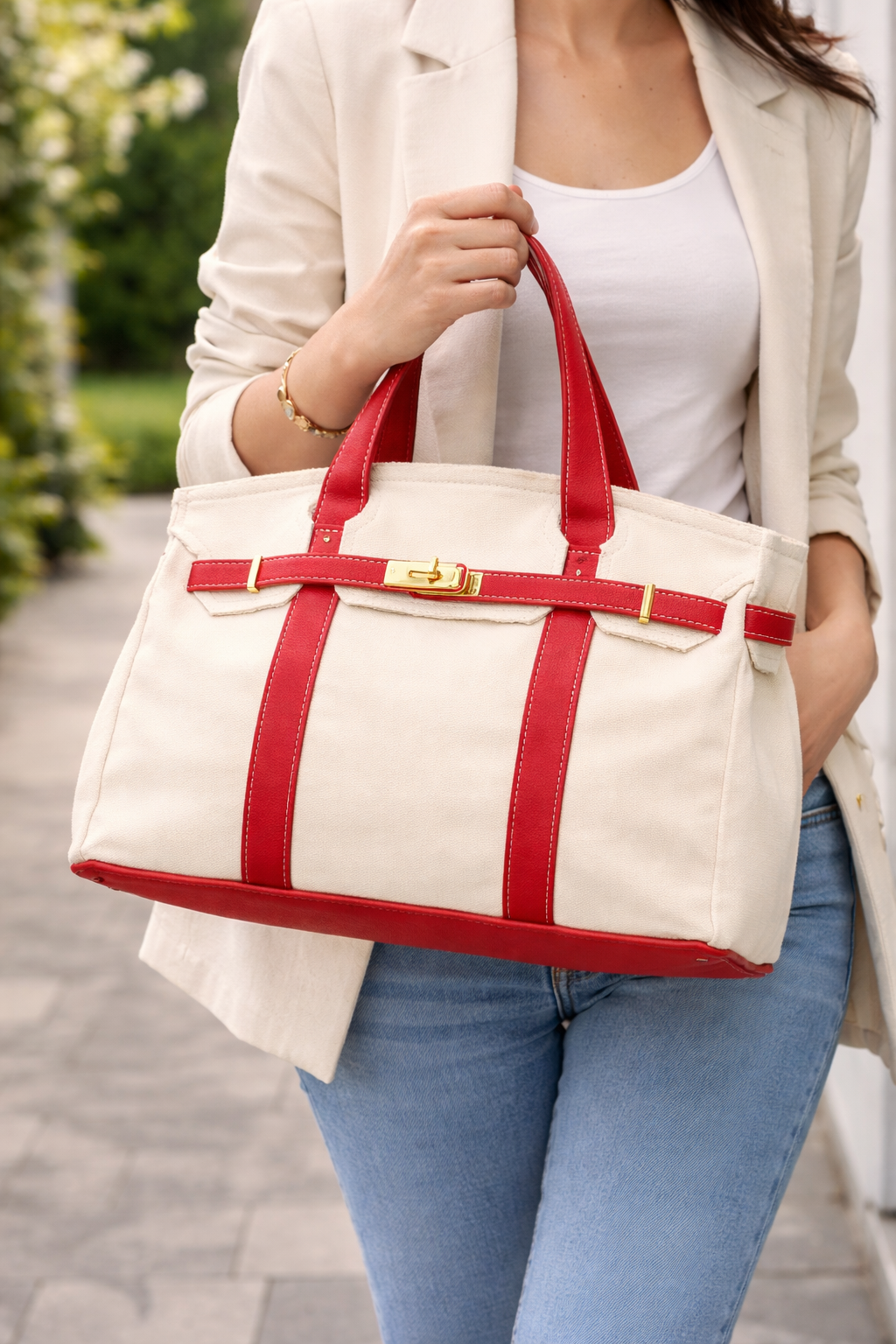 Person holding a white tote bag with red straps outdoors